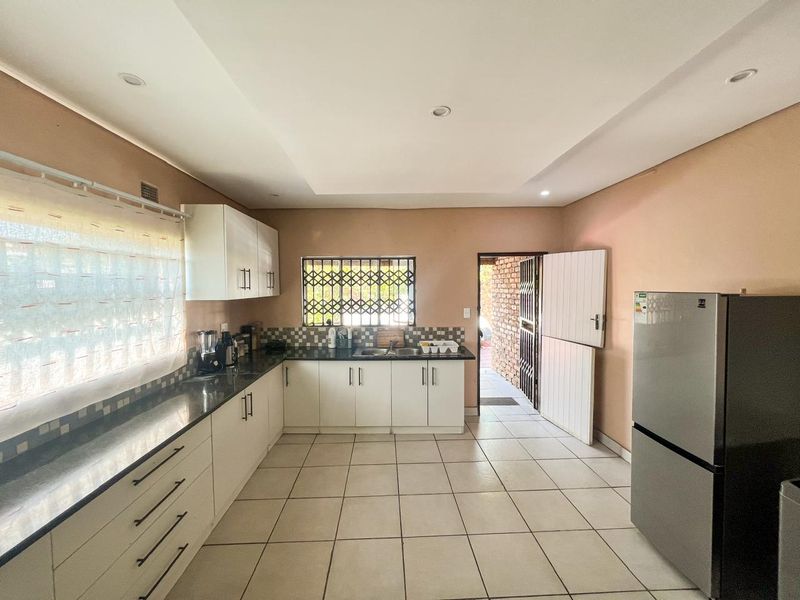 A functional kitchen featuring white cabinetry, dark granite countertops, tiled flooring, and a tiled backsplash, with direct access to an outdoor area.