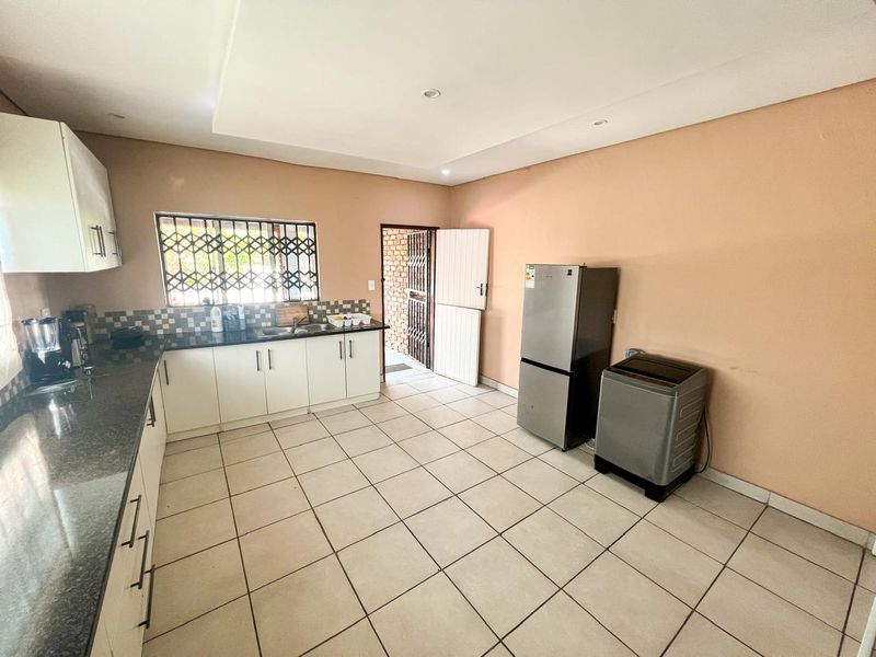 A functional kitchen featuring white cabinetry, dark granite countertops, tiled flooring, and direct access to an exterior area through a security gate.