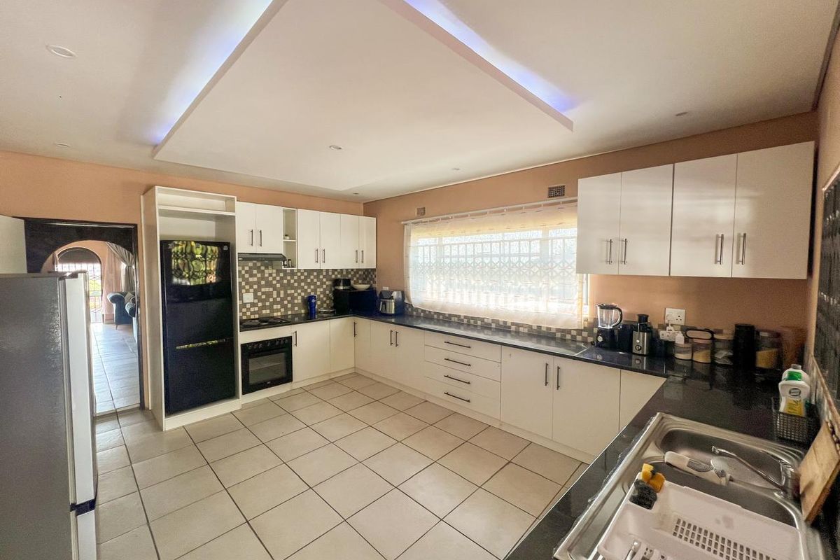 Spacious kitchen featuring white cabinetry, dark granite countertops, mosaic tile backsplash, built-in oven, hob, and a modern recessed ceiling feature with ambient lighting.
