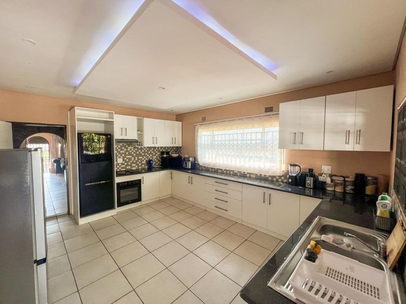 Spacious kitchen featuring white cabinetry, dark granite countertops, mosaic tile backsplash, built-in oven, hob, and a modern recessed ceiling feature with ambient lighting.