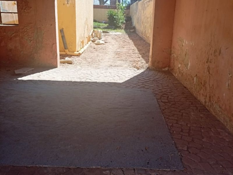 An open-plan garage space featuring cobblestone flooring and corrugated metal roofing, requiring significant maintenance and cosmetic repairs to the wall finishes.