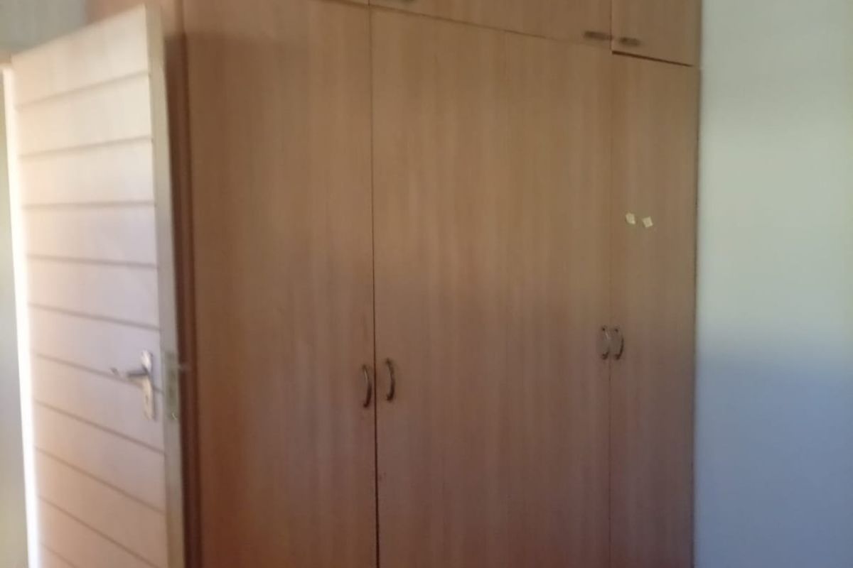 A bedroom featuring floor-to-ceiling built-in wooden cupboards and laminate flooring, presenting a functional space ready for personalization.