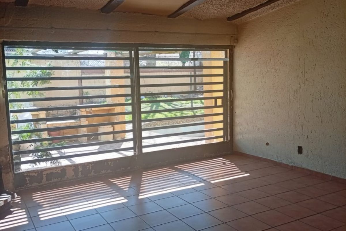 An empty living area featuring tiled floors, exposed ceiling beams, and a large security gate leading to the outdoor space.