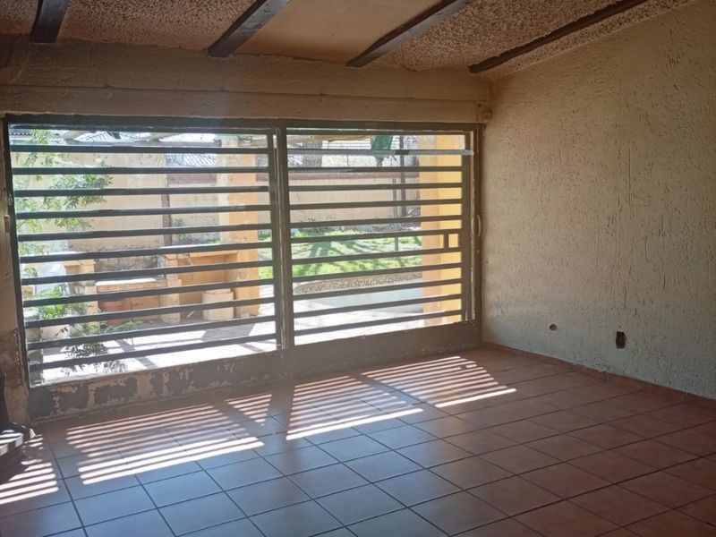 An empty living area featuring tiled floors, exposed ceiling beams, and a large security gate leading to the outdoor space.