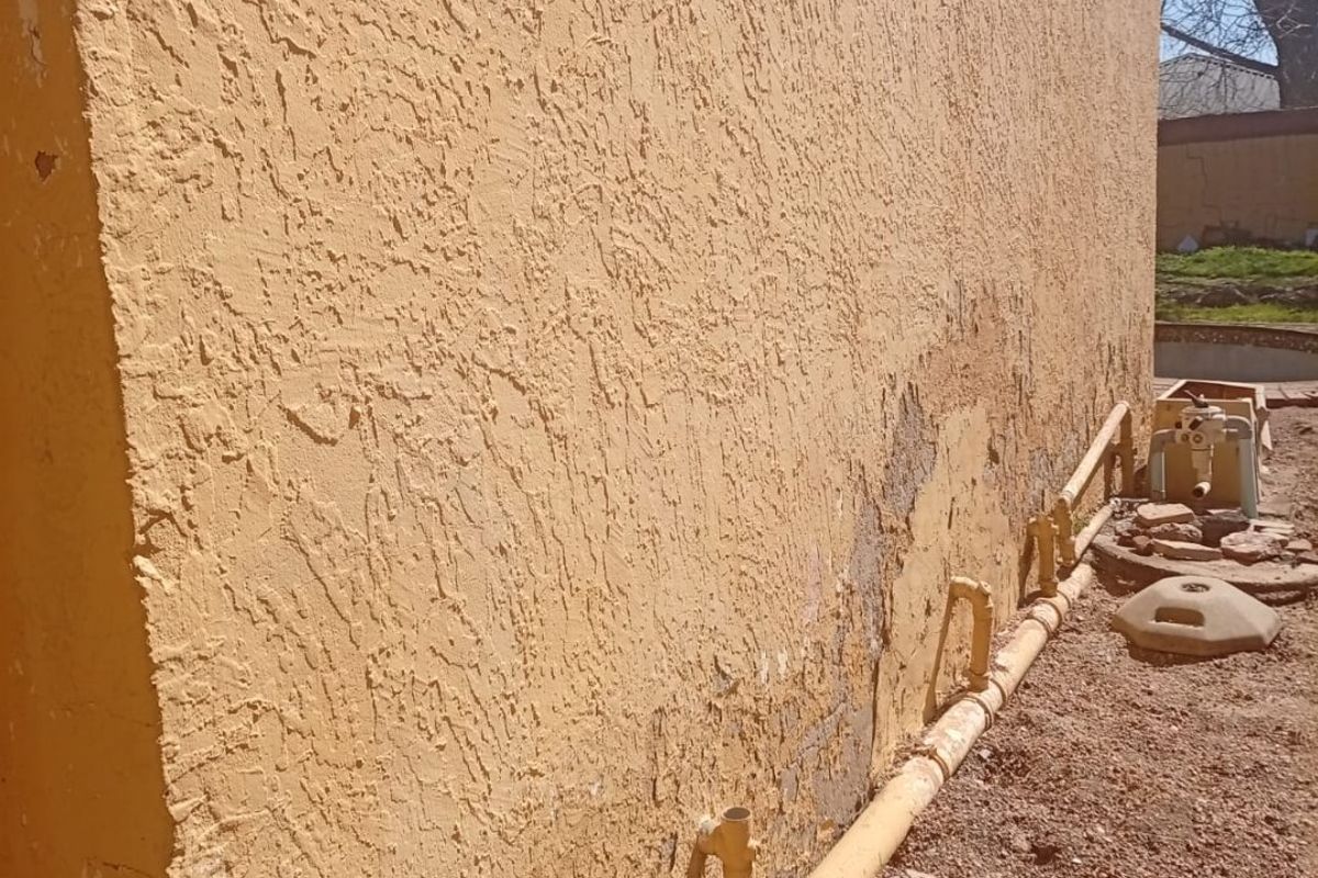 Side view of the exterior wall showing significant stucco deterioration, peeling finish, and exposed masonry, requiring maintenance and repair.