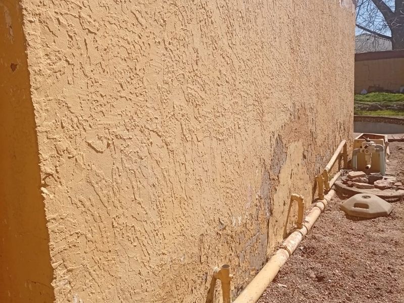 Side view of the exterior wall showing significant stucco deterioration, peeling finish, and exposed masonry, requiring maintenance and repair.