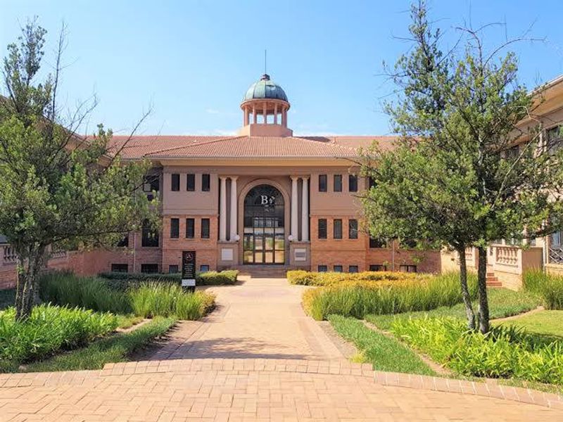 A well-maintained commercial building facade featuring a central cupola, brick exterior, and a paved entrance walkway surrounded by landscaped gardens.