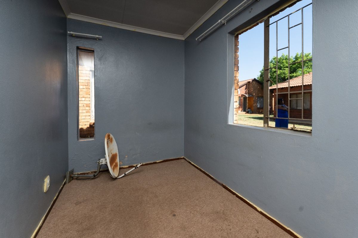 An empty bedroom featuring carpet flooring and security bars on the windows, requiring maintenance and cosmetic updates to restore its condition.