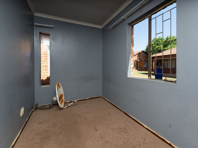 An empty bedroom featuring carpet flooring and security bars on the windows, requiring maintenance and cosmetic updates to restore its condition.