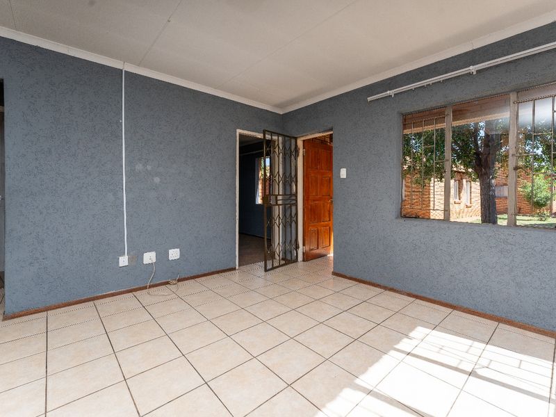 An empty living room featuring tiled flooring, security gate, and windows with burglar bars, offering a blank canvas for interior design.