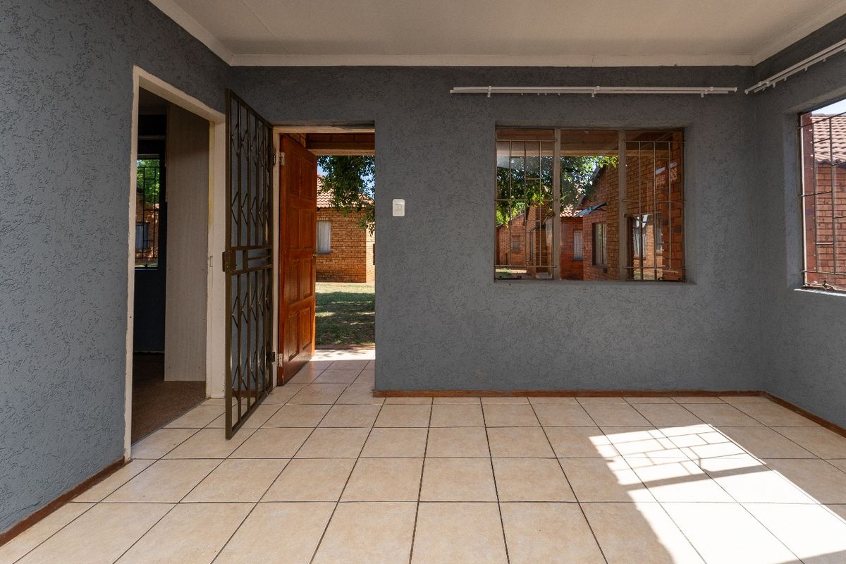 An empty living area featuring ceramic floor tiles, textured grey walls, and a security gate leading to the exterior.