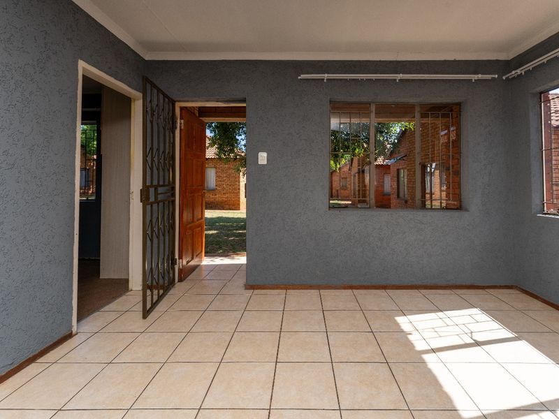 An empty living area featuring ceramic floor tiles, textured grey walls, and a security gate leading to the exterior.