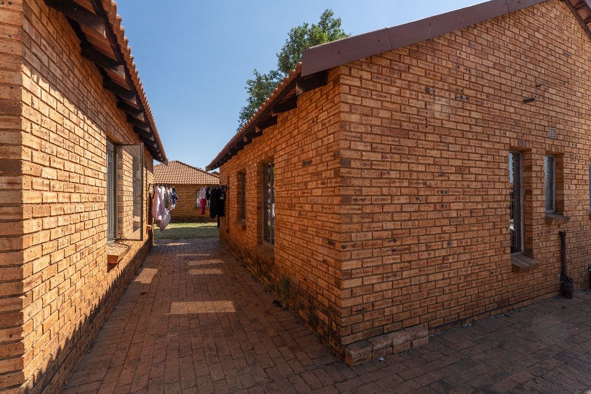 A view of the exterior rear area featuring face brick walls, a tiled roof, and a paved walkway between the apartment units.