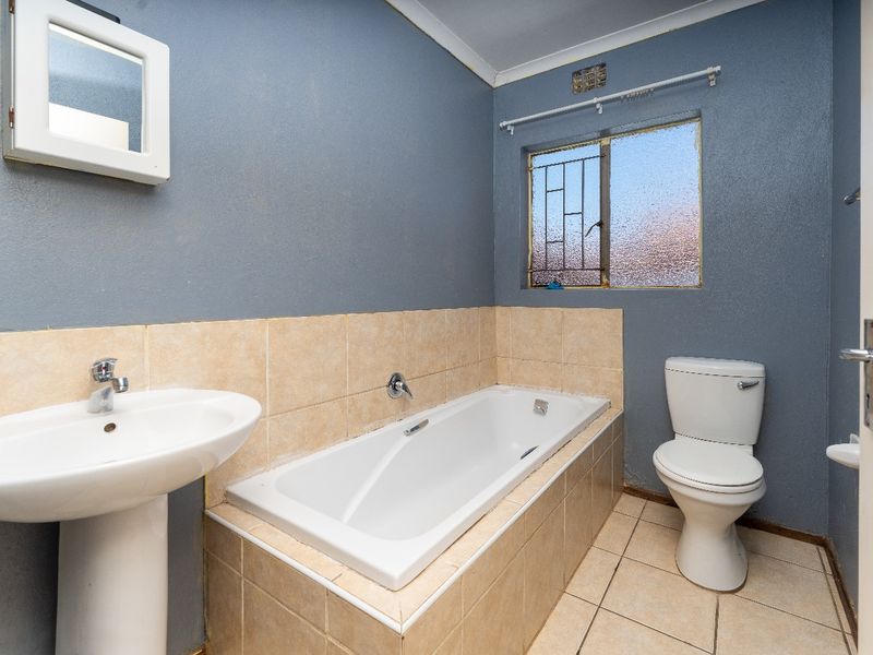 A functional bathroom featuring a pedestal basin, built-in bathtub, and toilet with tiled finishes and security bars on the window.