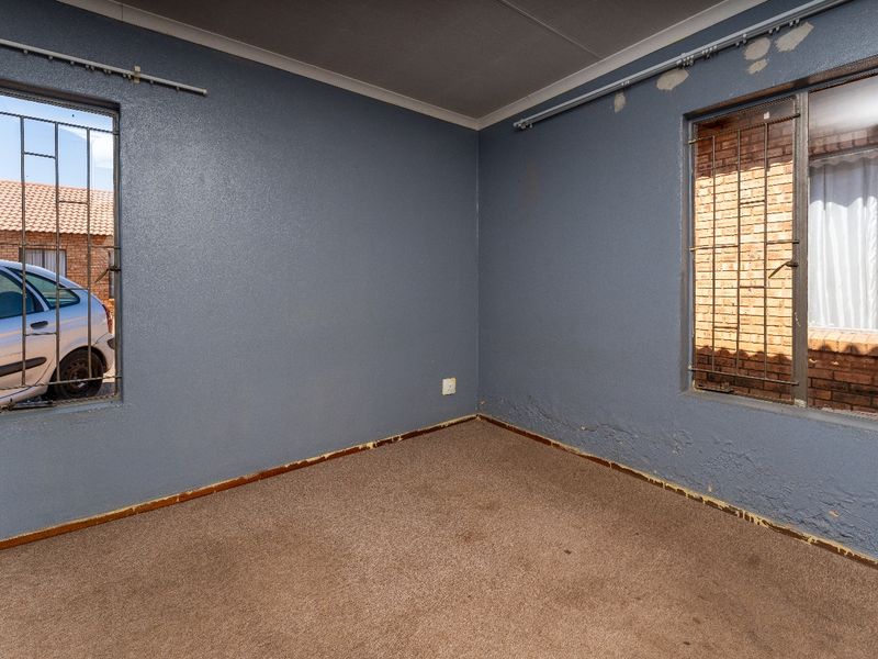 An empty bedroom featuring blue walls, carpet flooring, and security bars on the windows, requiring cosmetic updates and wall repairs.