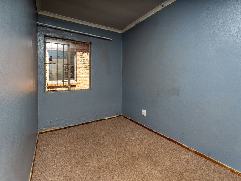 An empty bedroom featuring blue painted walls, carpeted flooring, and a window fitted with security bars.