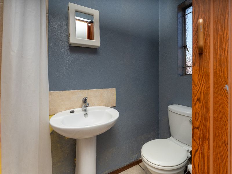 A compact bathroom featuring a pedestal basin, toilet, and shower area, requiring cosmetic updates to the wall finishes and overall presentation.