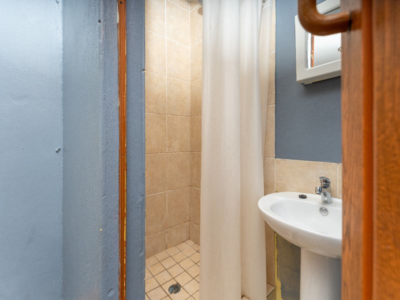 A compact bathroom featuring a pedestal basin and a tiled shower cubicle, currently requiring minor cosmetic finishing to the wall surfaces.