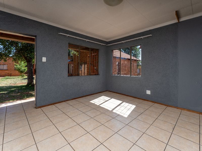 An empty living room featuring tiled flooring, textured grey walls, and security bars on the windows with direct access to the exterior.