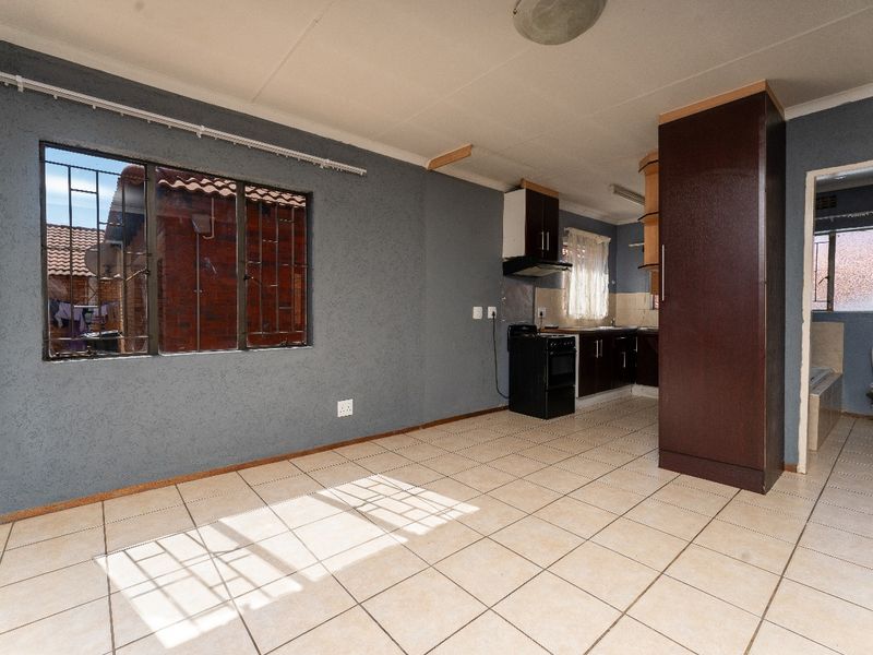 Open-plan living and kitchen area featuring tiled flooring, built-in cabinetry, and a freestanding stove, offering a functional layout in need of minor cosmetic updates.