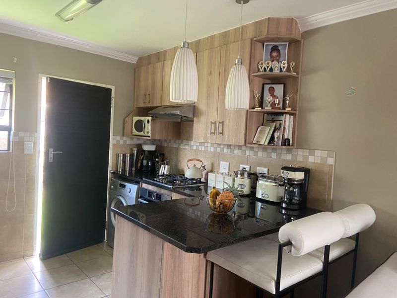A functional kitchen featuring wood-finish cabinetry, granite countertops, a gas hob, and an integrated oven, complemented by a tiled backsplash and modern pendant lighting.