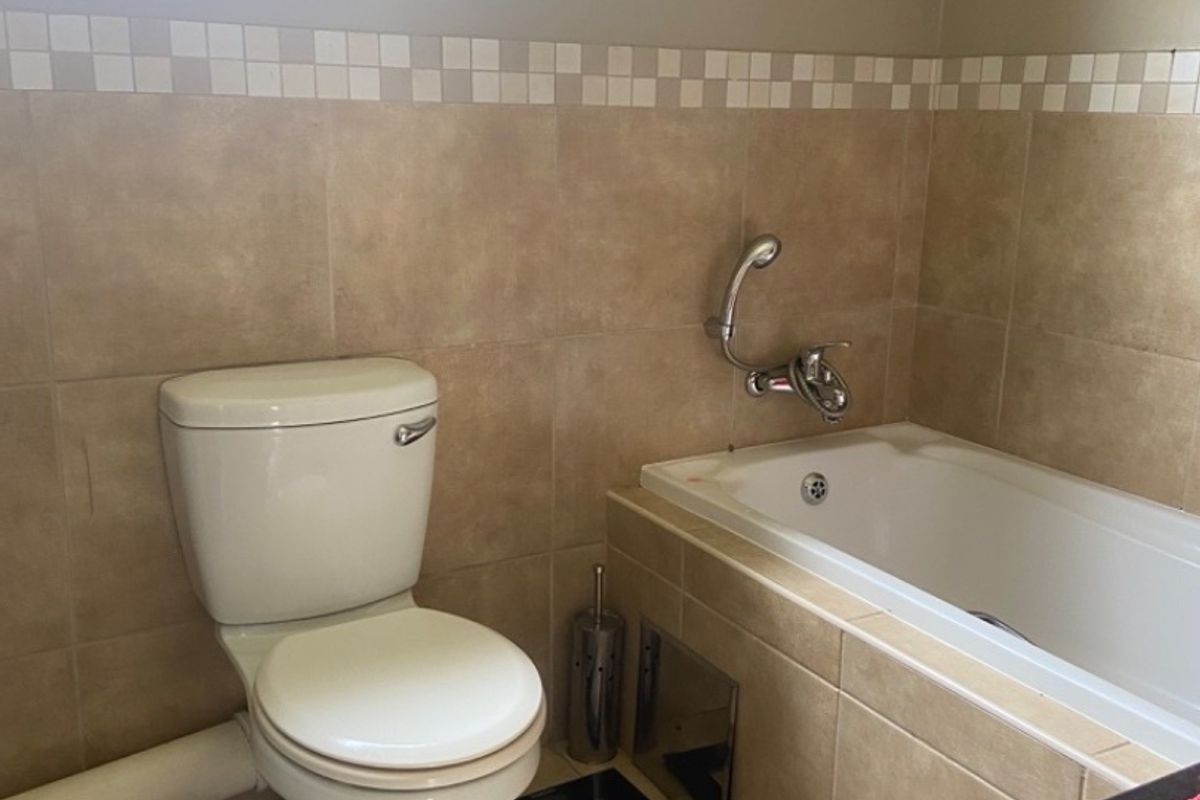 A functional bathroom featuring a bathtub with shower mixer, toilet, and neutral wall tiling with a decorative border.