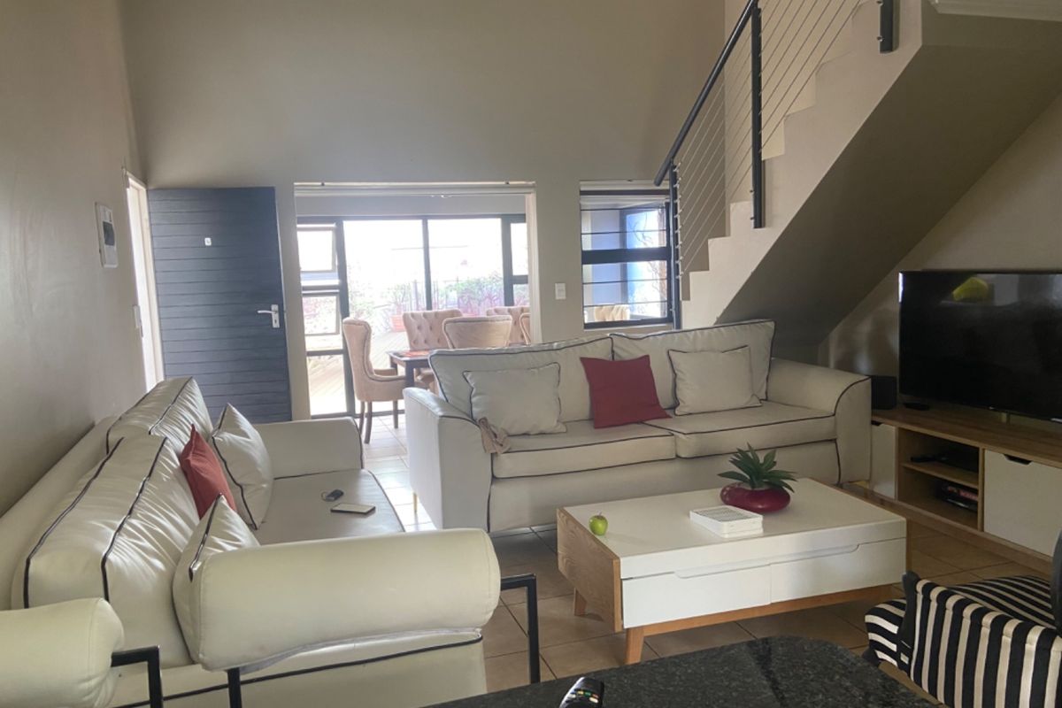 Open-plan living area featuring a staircase with metal balustrade, tiled flooring, and sliding glass doors leading to an outdoor patio space.