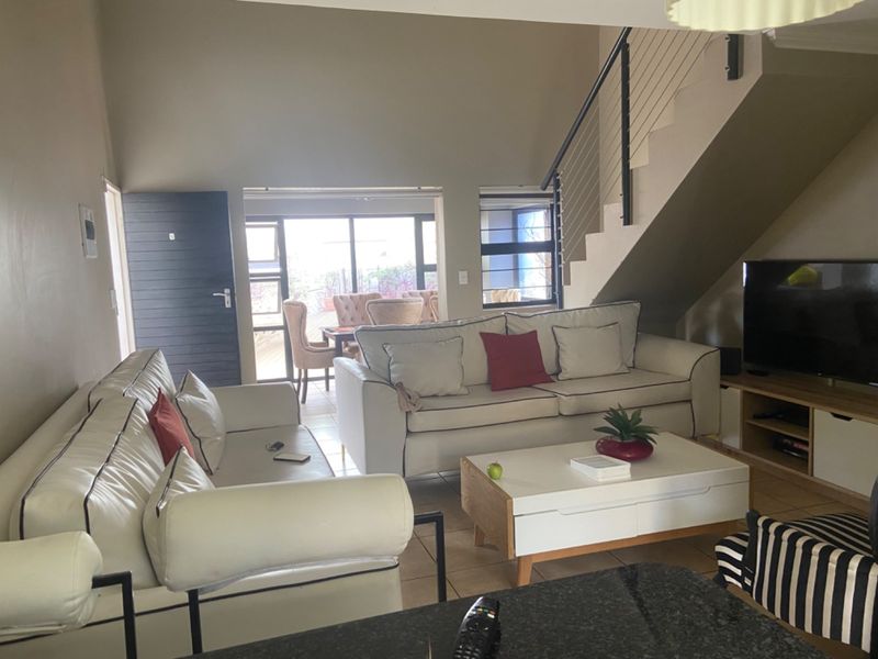 Open-plan living area featuring a staircase with metal balustrade, tiled flooring, and sliding glass doors leading to an outdoor patio space.