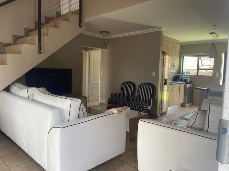 Open-plan living area featuring a staircase, tiled flooring, and a functional kitchen with built-in cabinetry and counter space.