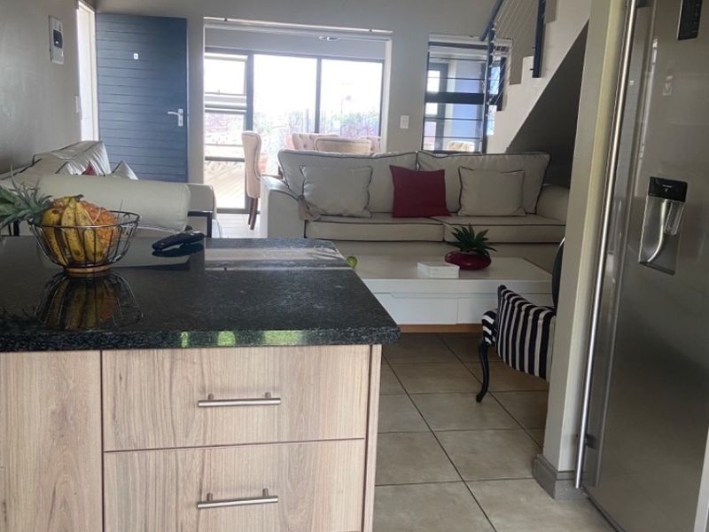 Open-plan living area featuring a kitchen island with granite countertops, tiled flooring, and a staircase leading to the upper level.