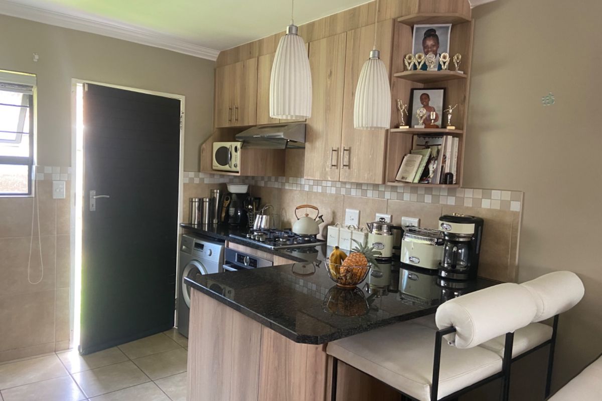 A functional kitchen featuring wood-finish cabinetry, granite countertops, a gas hob, and an integrated oven, with a breakfast nook and tiled flooring.