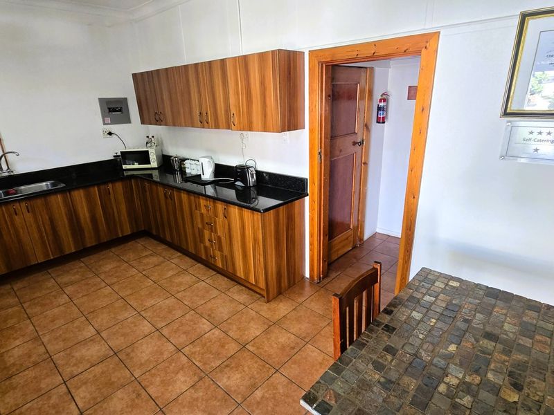 Functional kitchen featuring wood-look cabinetry, granite countertops, and tiled flooring, with direct access to an adjacent utility area.