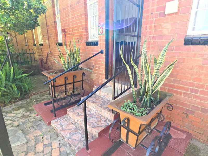 Front entrance of a brick house featuring tiled steps, metal handrails, and security gates.