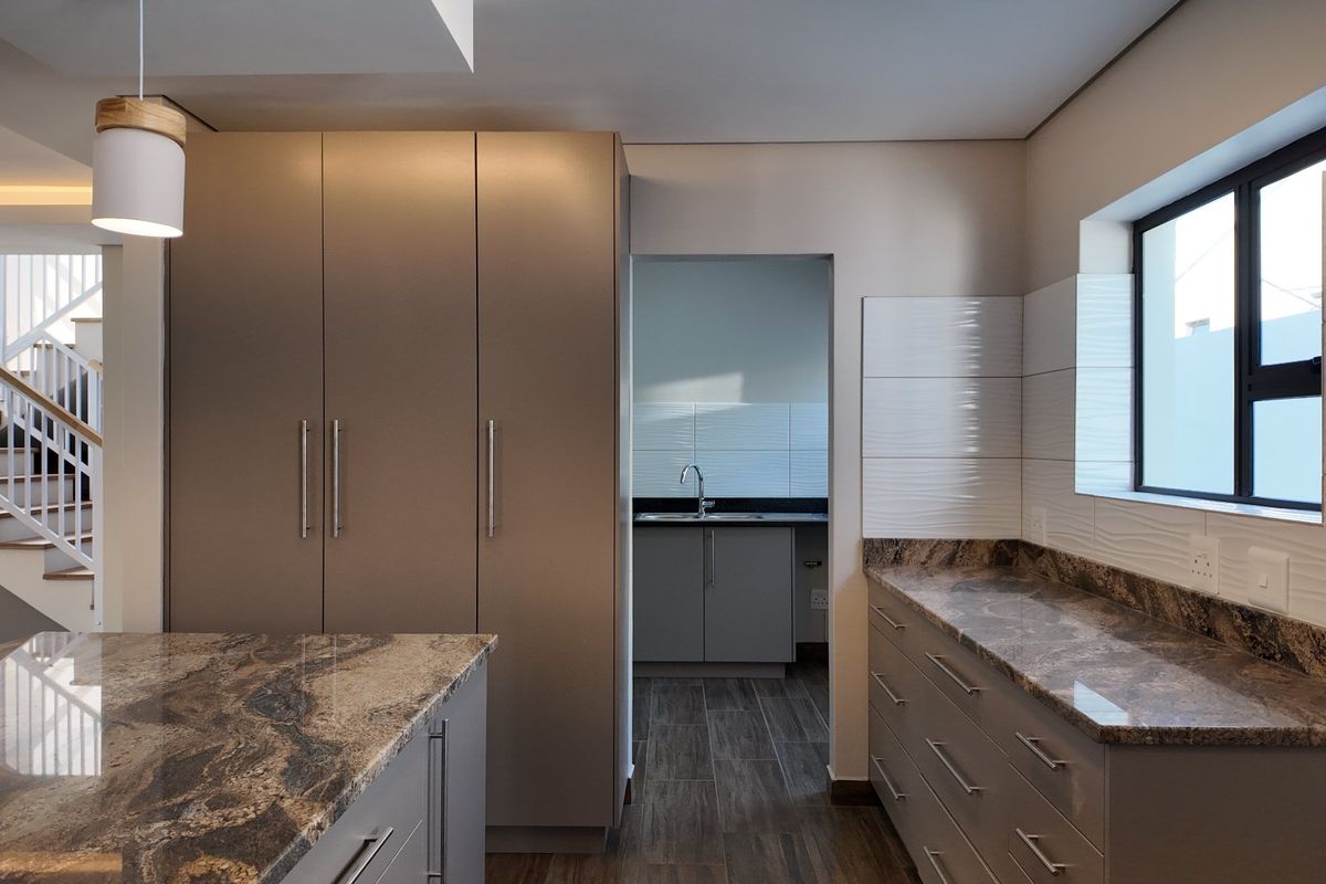 Modern kitchen featuring granite countertops, sleek built-in cabinetry, and a separate scullery area, adjacent to an open staircase.