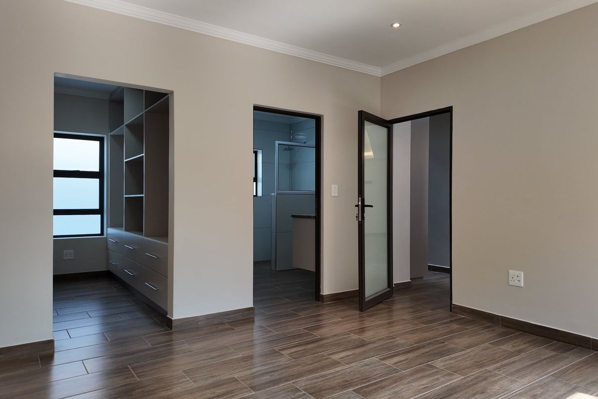 A spacious, modern bedroom featuring wood-look tiled flooring, recessed lighting, and an adjoining walk-in closet and en-suite bathroom.