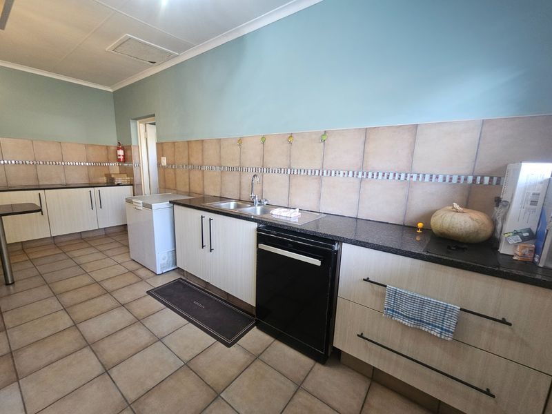 A functional kitchen featuring laminate cabinetry, granite countertops, a double sink, and tiled splashbacks with neutral ceramic floor tiles.