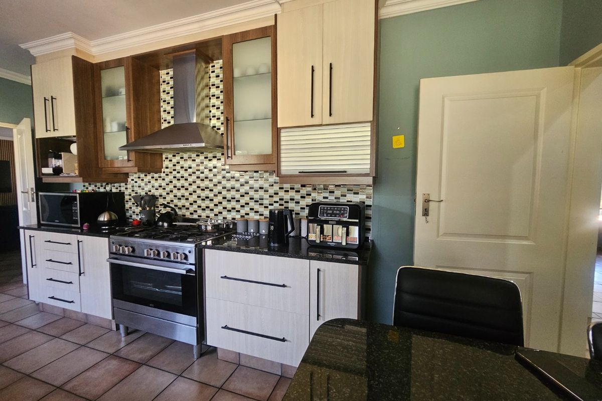 A well-appointed kitchen featuring granite countertops, a gas stove with stainless steel extractor, mosaic backsplash, and modern two-tone cabinetry.