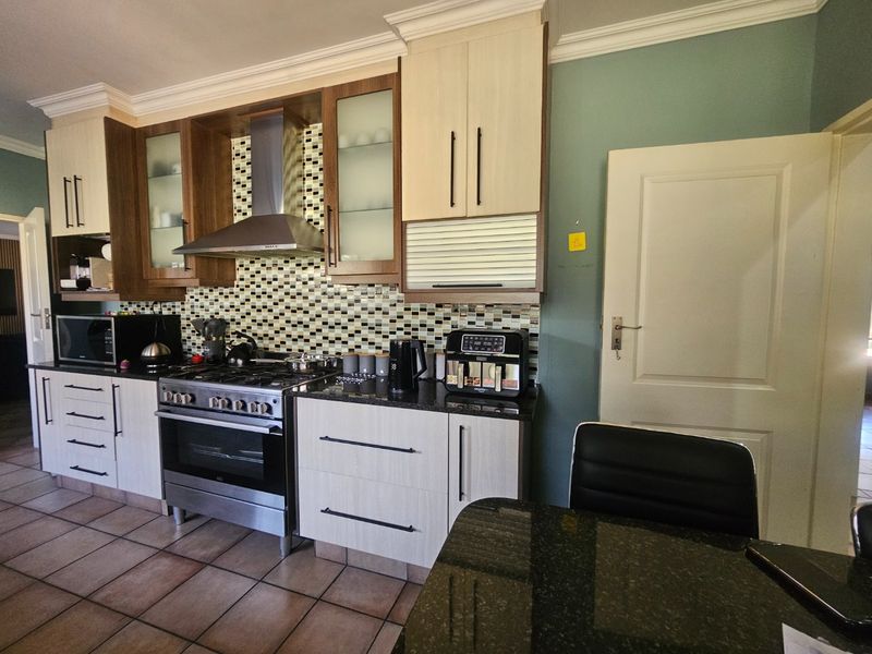 A well-appointed kitchen featuring granite countertops, a gas stove with stainless steel extractor, mosaic backsplash, and modern two-tone cabinetry.