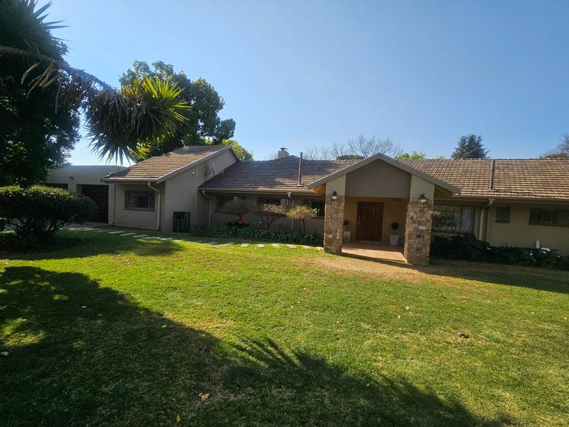 A well-maintained single-story family home featuring a tiled roof, stone-clad entrance pillars, and a spacious front lawn with a paved walkway.