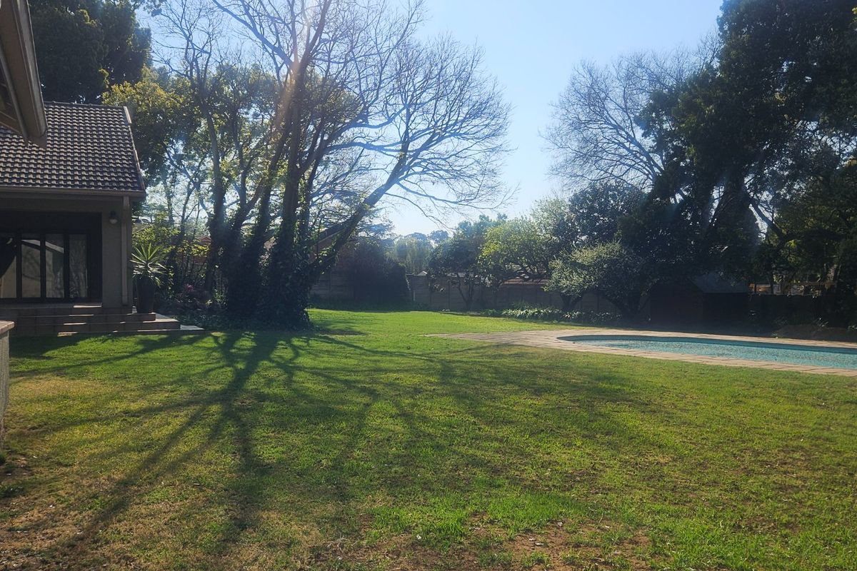 Spacious rear garden featuring a large lawn, mature trees, and a swimming pool with a paved surround.
