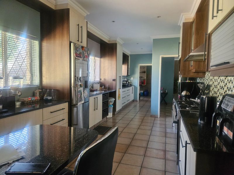 Spacious kitchen featuring granite countertops, extensive built-in cabinetry, gas hob with extractor fan, and tiled flooring, leading to a secondary utility area.