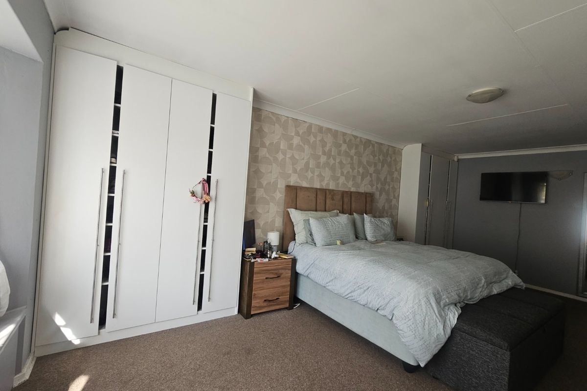 Spacious bedroom featuring built-in wardrobes, a decorative feature wall, and neutral carpeting, offering a comfortable and functional living space.