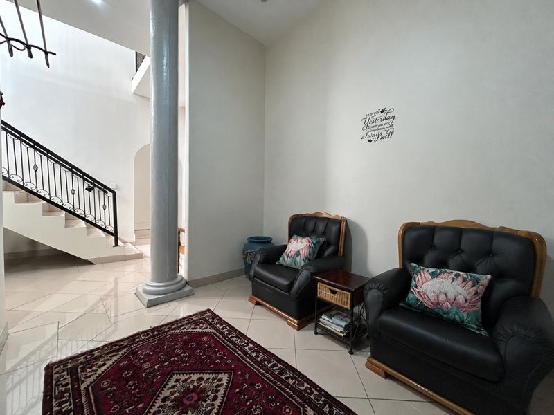 Spacious entrance hall featuring tiled flooring, a prominent structural column, and a staircase with a decorative wrought iron balustrade.