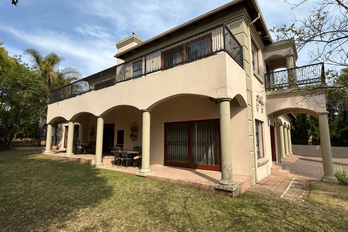 Rear view of a two-story house featuring a spacious covered patio, upper-level balcony with wrought iron railings, and classic architectural columns.