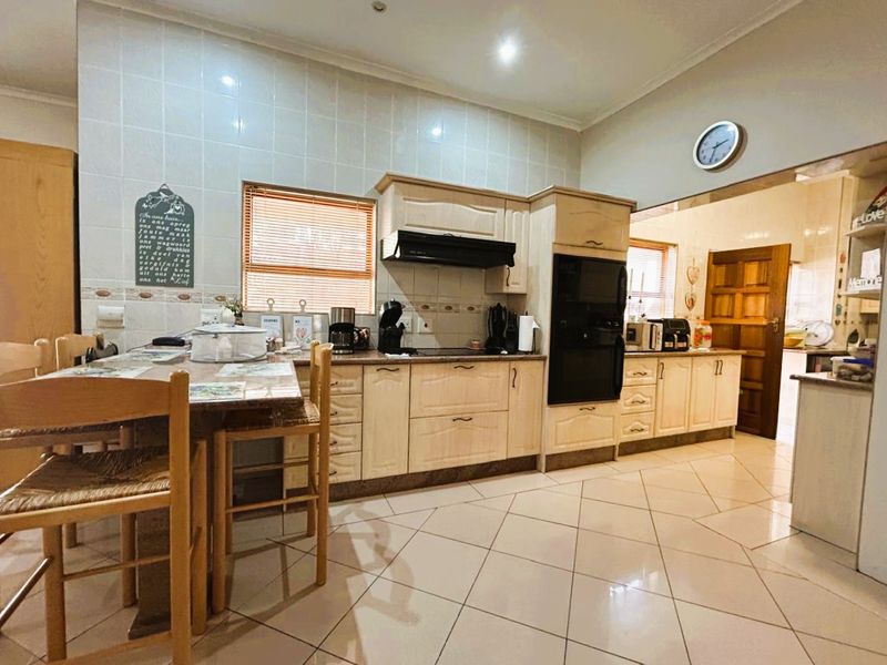 A functional kitchen featuring light-toned cabinetry, tiled backsplash, built-in oven, and ceramic hob, with tiled flooring throughout.
