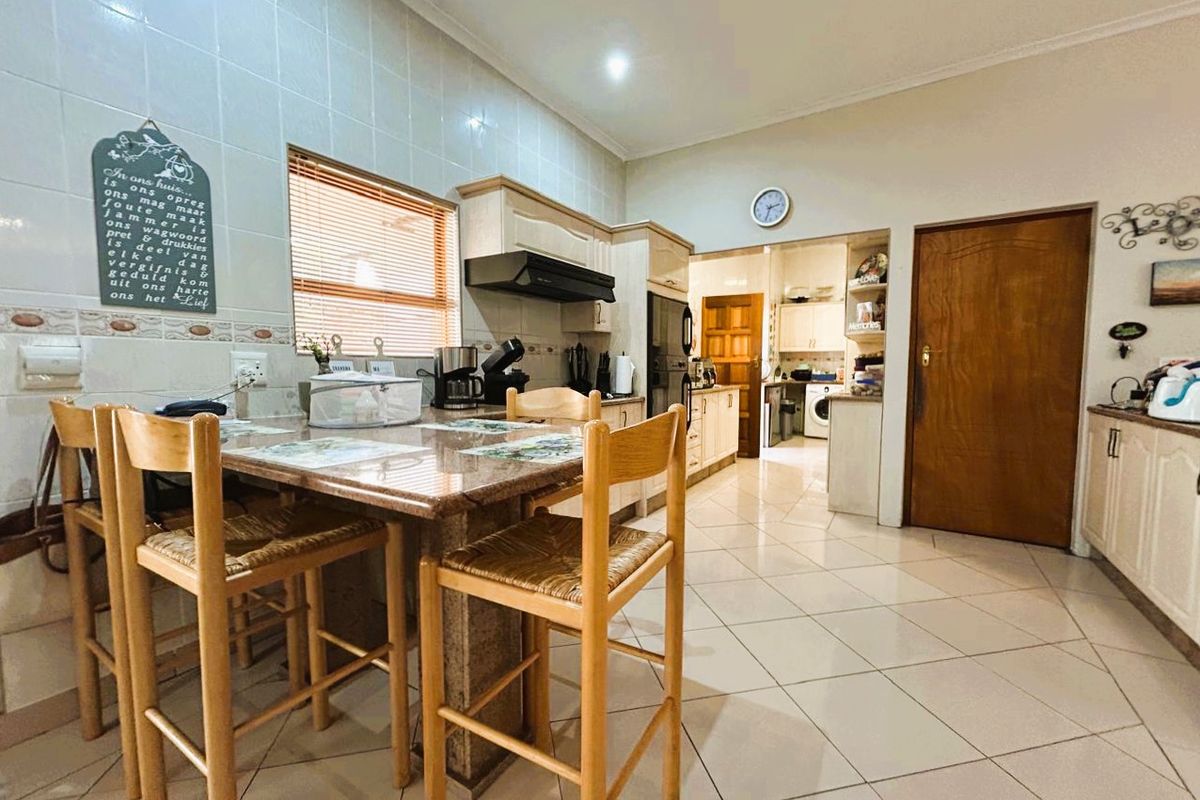 A functional kitchen featuring granite countertops, tiled flooring, and built-in cabinetry, with an adjacent scullery area visible through the doorway.