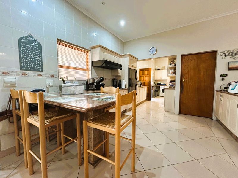 A functional kitchen featuring granite countertops, tiled flooring, and built-in cabinetry, with an adjacent scullery area visible through the doorway.