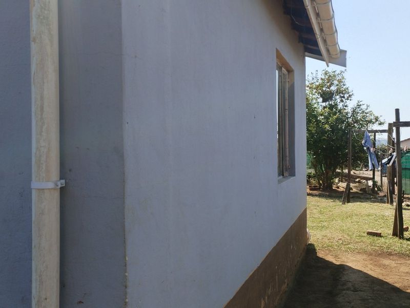 A view of the rear exterior wall of the house, featuring a downpipe, guttering, and a window, with a garden area visible in the background.
