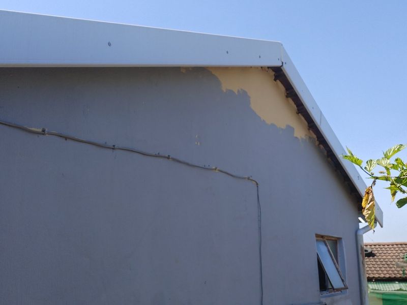 Exterior view of the house gable end showing peeling paint and exposed plaster on the wall surface.