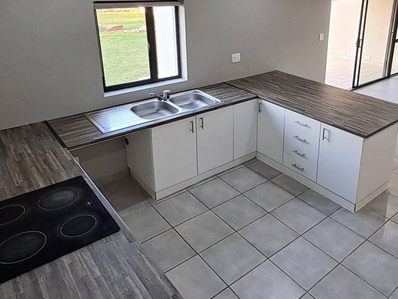 Modern open-plan kitchen featuring white cabinetry, laminate countertops, a built-in electric hob, and a double bowl sink with tiled flooring.